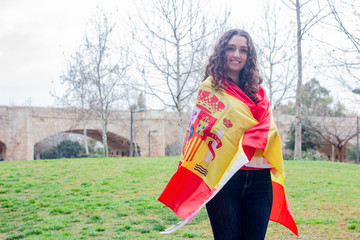 Portrait of pretty young woman holding a spanish flag, Spain, in the park, orange sweater and...