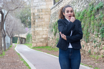 Portrait of pretty caucasian bussiness woman model holds hands in fists under chin, looks worried, has eyes popped out, being frightened by unexpected news, in the park, white shirt and black jacket,