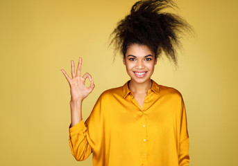 Young girl says good job or well done, makes okay gesture. Photo of african american girl on yellow...
