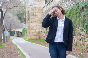 Portrait of pretty caucasian bussiness woman model touches his forehead and having headache, in the park, white shirt and black jacket, long curly hair. Place for your text in copy space.