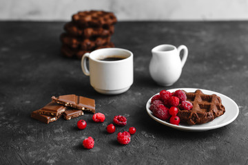 Homemade chocolate waffles with cocoa and powdered sugar on a plate with raspberries and chocolate on a dark background space for text