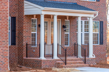 Portico leading to the entrance of brick covered building, with a roof structure over a walkway,...