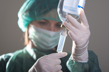 Close up of female doctor with medical mask and gloves preparing a drip