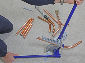A man using a pipe bender to create a bend in copper pipe.