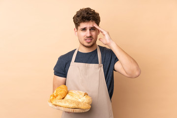 Male baker holding a table with several breads isolated on beige background unhappy and frustrated with something. Negative facial expression