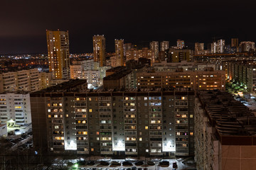 Obraz premium Glowing windows of multi-storey residential buildings. Residential areas on a winter night. A lot of parked cars in the yards