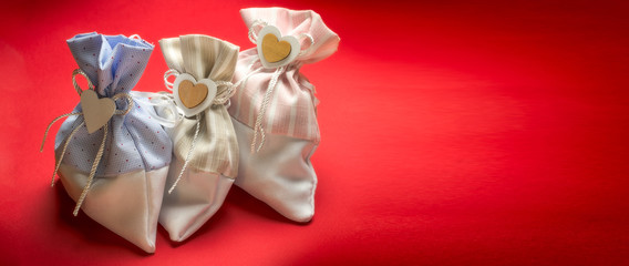 Three rag gift bags with a heart and a bow on a red background with copy space. Holiday concept.