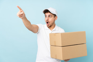 Delivery caucasian man isolated on blue background pointing away