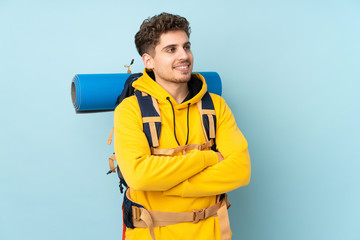 Young mountaineer man with a big backpack isolated on blue  background looking to the side