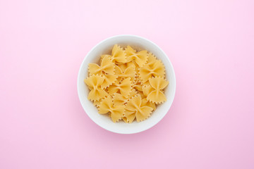 A pile of farfalle pasta in a small white bowl on a pink background