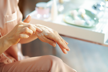 woman applying hand cream at home in sunny winter day