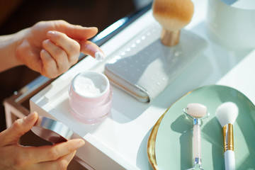 modern woman using cosmetic jar on table with toiletries