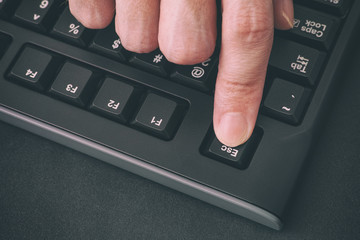 Person's finger pressing Escape key on a black computer keyboard