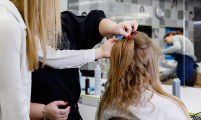 Hairstyle in Hair training center for hairdresser stylist. Hairdresser making hairstyle to blonde hair woman with long hair in beauty salon. Teacher trainer help to hairdresser making hairstyle.