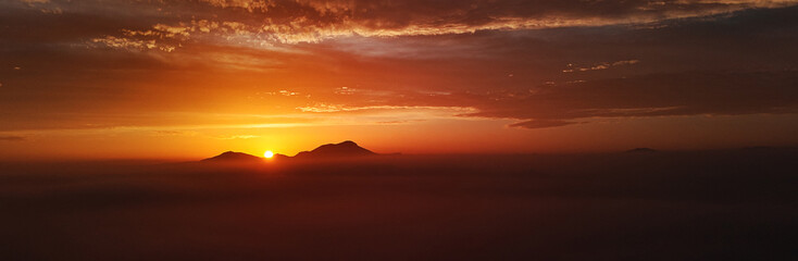 Panoramic view horizon over land and glowing sunlight through mountains
