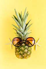Hipster pineapple in sunglasses on yellow background. Summer background. Flat lay, top view.