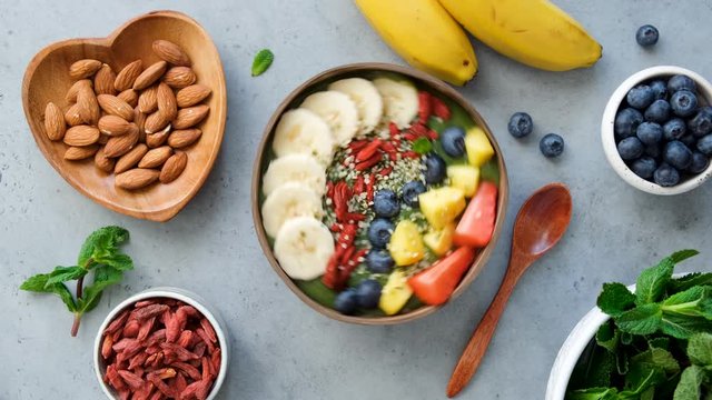 Green smoothie bowl with superfoods goji chia mango banana blueberry and strawberry. Top view. Rotating smoothie bowl on concrete background 4k footage