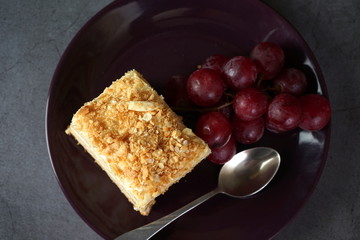 Cake of many layers and grapes on a dark plate