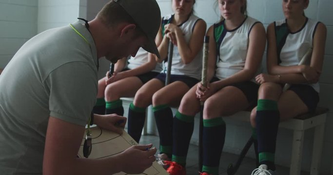 Hockey coach explaining game plan with female players in locker room