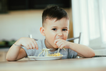 A child in the kitchen at the table eats macaroni and cheese very appetizing