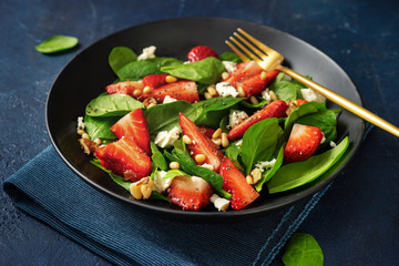 Close up of strawberry salad with spinach, feta ans nuts on blue background