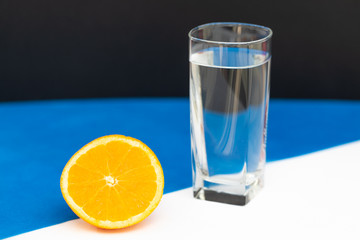  glass of water stands next to a cut open orange on a white-blue background
