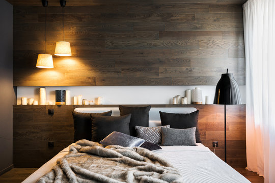 The interior of a stylish bedroom in dark colors. Wooden walls, dark linens, and lighting.
