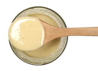 Sesame butter, paste tahini in wooden spoon and glass jar isolated on white background, top view