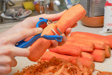 Children's hands peel carrots with a knife for cleaning. Nearby lies a bunch of carrot peels.