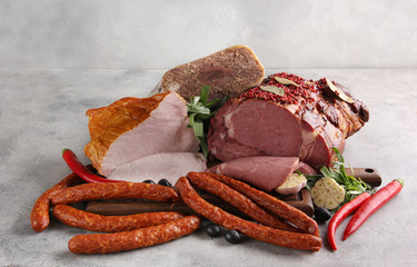 Assorted meat. Beef, pork, carbonate, sausages with garlic, olive, herbs and chili pepper on a wooden board. Light background. Background image, copy space