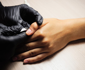 A manicurist, wearing black gloves, removes the cuticle on his thumb. Cosmetology, hand care, manicure.