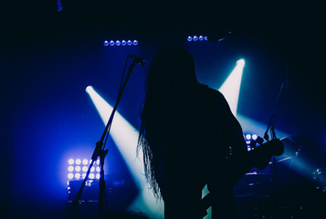 Basist, member of the metal band, performing live on stage. Silhouette and blue stage lights