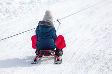 Fototapeta na wymiar Kids with sledge climbing at the snowy hill on winter park in Bakuriani