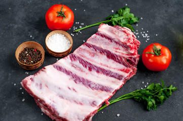 raw pork ribs with spices, tomatoes and herbs on a stone background