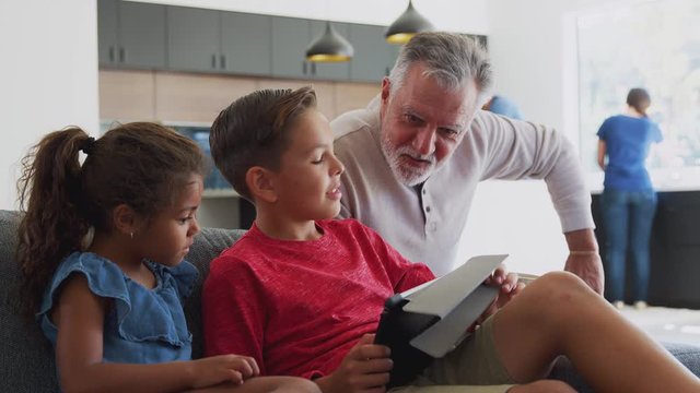 Grandfather Playing Video Games With Grandchildren On Digital Tablet At Home