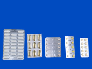Capsules and pills packed in blisters on blue background
