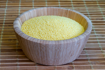 Dry couscous close-up in a wooden bowl on a bamboo stand. Concept of Oriental cuisine dishes