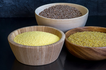 Cereals couscous, bulgur, red lentils in wooden bowls on a black background. Concept of Eastern cuisine dishes