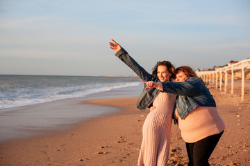 Back view of two freinds , plus size with  thin  girls walking on the spring beach. Fat woman with...