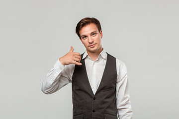 Young businessman in a white shirt and grey vest asking to call him with a hand gesture