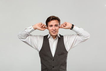 Irritated young businessman in a white shirt closing his ears to stop noise