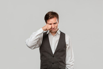 Handsome man in a white shirt and grey vest crying because he faces some problems need to be addressed
