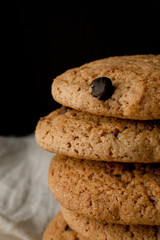 Oat cookies with chocolate on white textile over black background, closeup