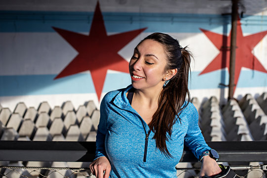 close up portrait of beautiful Hispanic woman wearing blue athletic gear is stretching happily for better health at an outdoor park on a sunny day. 