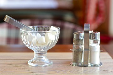 lump sugar in crystall vase sugar tongs solt and pepper closeup photo on cafe interior background