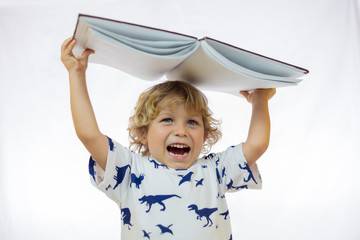 Little boy between 4 and 5 years old holding a book over his head while smiling