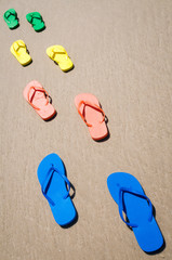 Group of flip-flops in bright summer colors walking along smooth sand beach