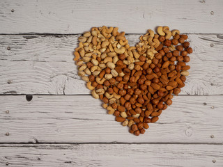 Almonds, hazelnuts, cashews and pistachios nuts scattered on a white wooden table in the shape of a heart top view with copy  space.