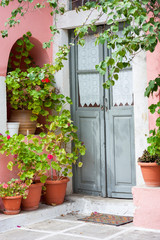 Empty view of quaint Mediterranean doorway with pink stucco walls framed by potted geranium plants and vines