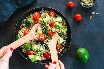 Hands mixing healthy salad with bulgur, avocado, spinach and cherry tomatoes. Top view.